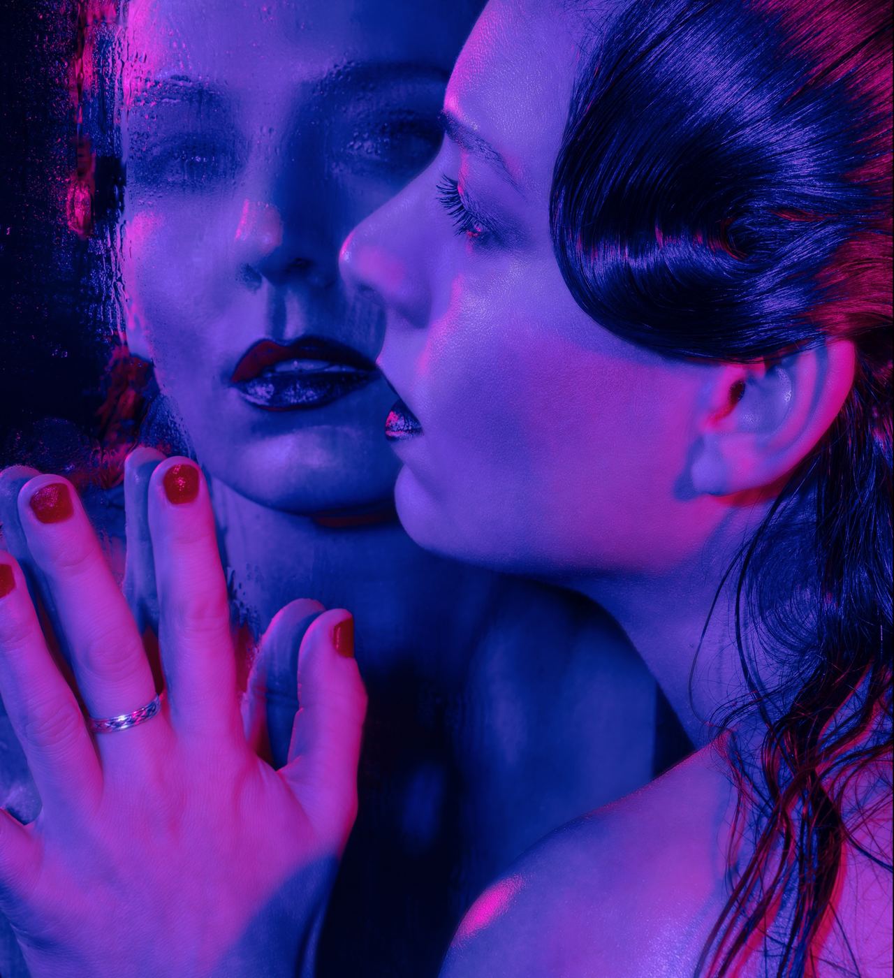 Portrait against wet glass in blue and magenta light