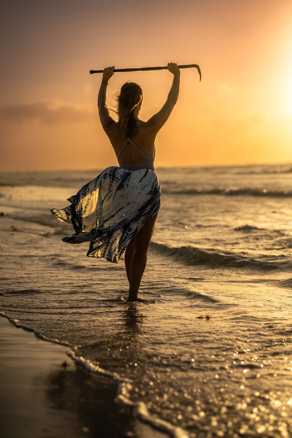 Woman at the shoreline at sunset, arms raised