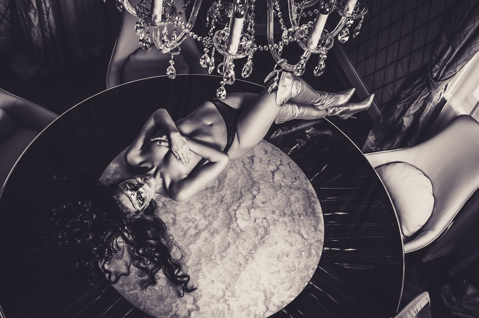 Boudoir portrait with mask on a marble table under a chandelier