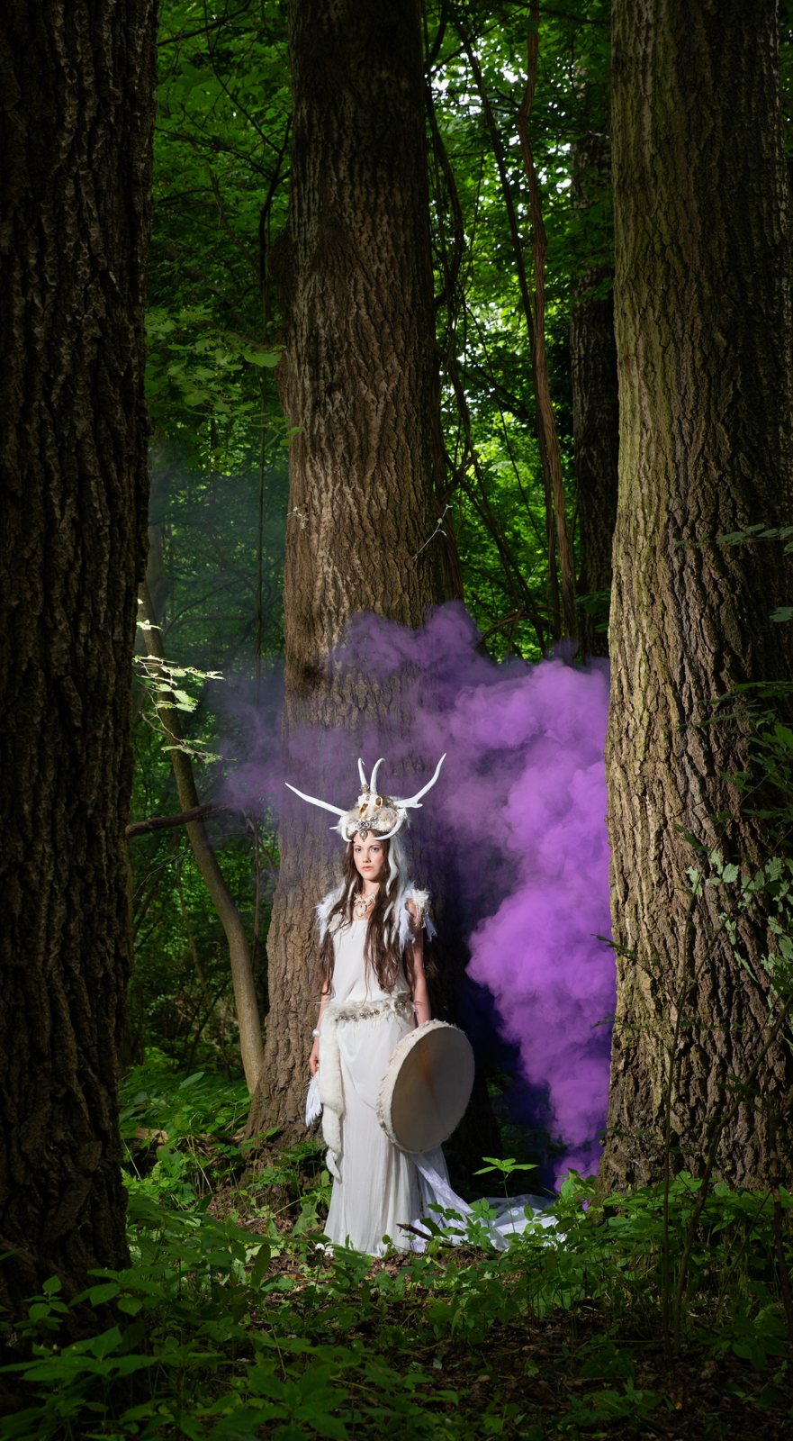 White goddess with antler crown and purple smoke in the forest